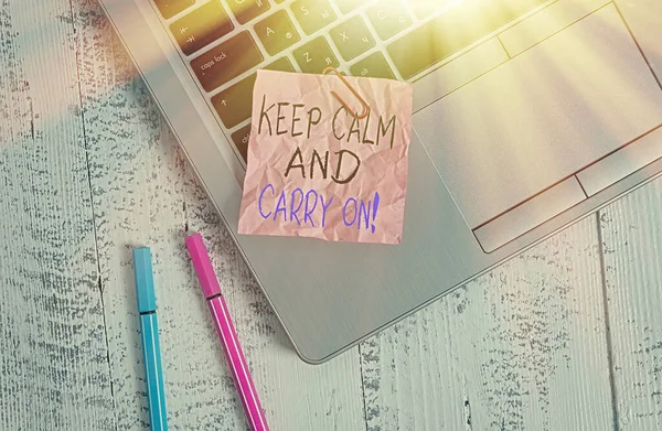 Conceptual hand writing showing Keep Calm And Carry On. Business photo text slogan calling for persistence face of challenge Metallic laptop crushed colored paper note pens lying wooden table.