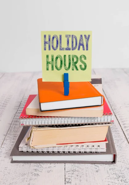 Text sign showing Holiday Hours. Conceptual photo Overtime work on for employees under flexible work schedules pile stacked books notebook pin clothespin colored reminder white wooden. — Stock Photo, Image