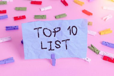 Top 10 Listesini gösteren kavramsal el yazısı. Belirli bir listedeki en önemli ya da en başarılı on öğeyi gösteren iş fotoğrafı. Renkli çamaşır iğnesi kağıtları boş hatırlatıcı pembe zemin ofisi..