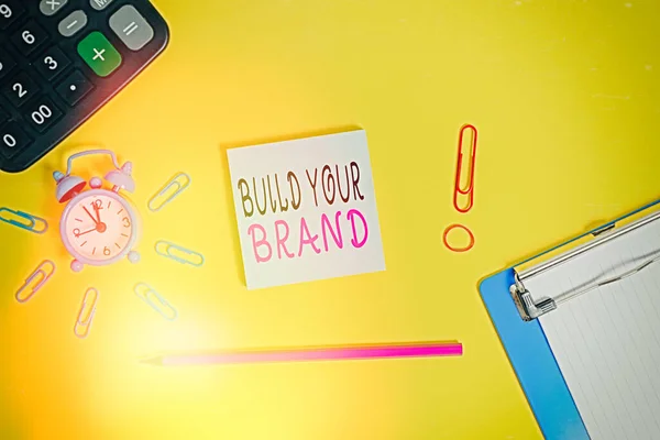 Handwriting text writing Build Your Brand. Concept meaning enhancing brand equity using advertising campaigns Alarm clipboard calculator clips band pencil notepad colored background. — Stock Photo, Image