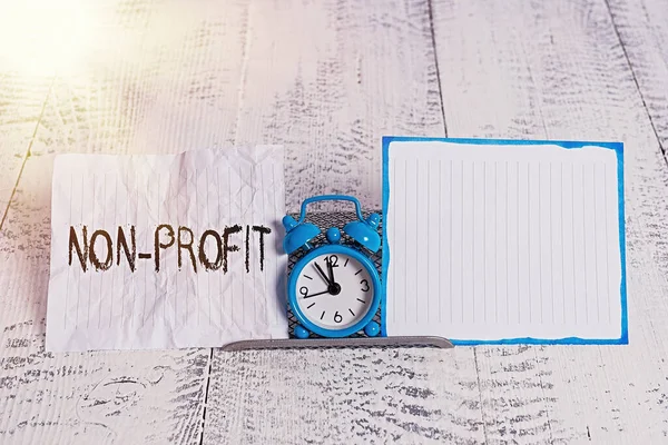 Conceptual hand writing showing Non Profit. Business photo text type of organization that does not earn profits for its owners Alarm clock tilted above buffer wire in front of notepaper.