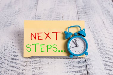 Kelime yazma metni Sonraki Adımlar. Bir şeyi bitirdikten sonra yapmak ya da planlamak için iş konsepti. Mini mavi alarm standı tampon telin üzerine eğilmiş. Not kağıdının önünde..