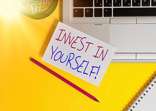 Word writing text Invest In Yourself. Business concept for nvesting in a coach or a training to learn new things Laptop pencil squared paper sheet clips container spiral colored background.