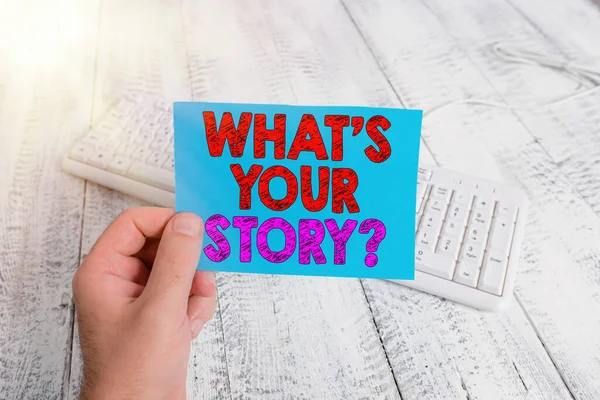 Tekst pisma odręcznego What Is Your Storyquestion. Koncepcja oznacza sposób zadawania pytań demonstrujących o przeszłych wydarzeniach życiowych człowiek trzyma kolorowe przypomnienie kwadratowy kształt papieru biały klawiatura drewniana podłoga. — Zdjęcie stockowe