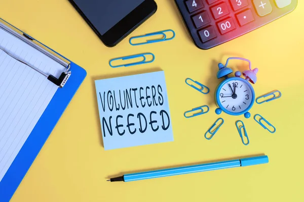 Handwriting text Volunteers Needed. Concept meaning need work or help for organization without being paid Alarm clipboard clips smartphone marker calculator notepad color background. — Stock Photo, Image