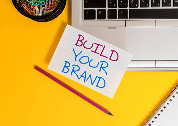 문자를 사용하면 브랜드를 만들 수있다. 광고 캠페인을 사용하여 브랜드의 공정성을 강화하기 위한 비즈니스 컨셉 랩탑 연필 제곱 종이 시트 클립 컨테이너 스파이럴 색 배경. — 스톡 사진