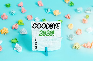 Mesaj işareti 2020 'ye güle güle diyor. Kavramsal fotoğraf geçen yılın sonunda ya da ayrılırken iyi dileklerini ifade eder Renkli buruşmuş kağıtlar boş hatırlatıcı mavi zemin çamaşır mandalı.