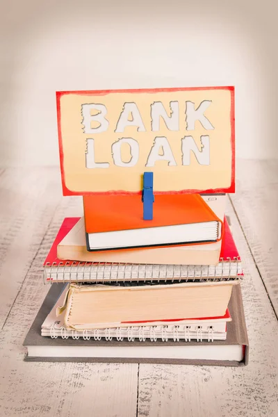 Handwriting text writing Bank Loan. Concept meaning an amount of money loaned at interest by a bank to a borrower pile stacked books notebook pin clothespin colored reminder white wooden.