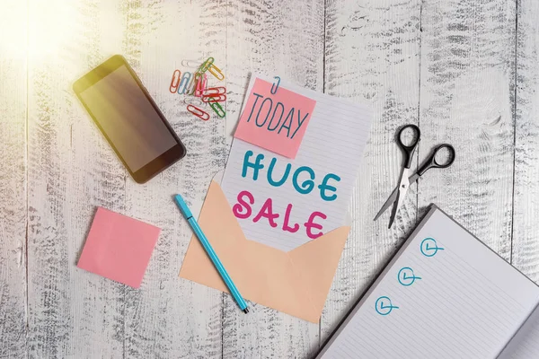 Text sign showing Huge Sale. Conceptual photo putting products on high discount Great price Black Friday Envelope sheet smartphone notes pen notepad clips scissors wooden back. — Stock Photo, Image