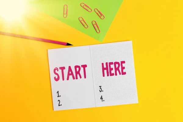 Text sign showing Start Here. Conceptual photo telling someone this is beginning point to go from to destination Blank paper sheet pencil clips smartphone two notepads colored background.