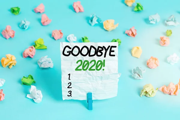 Text sign showing Good Bye 2020. Conceptual photo express good wishes when parting or at the end of last year Colored crumpled papers empty reminder blue floor background clothespin.