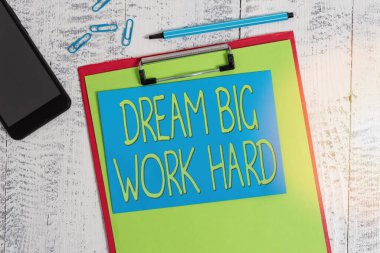Dream Big Work Hard 'ı gösteren bir not yazıyorum. İş fotoğrafı gösterimi Kendine inan ve hayalleri ve hedefleri takip et. Kağıt kalem, raptiye, akıllı telefon ahşap arka plan..