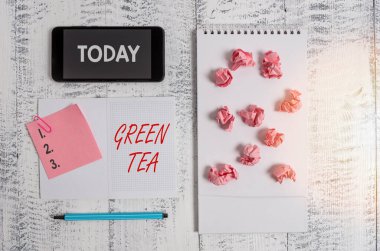 Kelime yazma Green Tea. Kamelya sinensis yaprakları ve tomurcuklarından yapılan çay tipi iş konsepti. Kare spiral defter, akıllı telefon, kağıt, ataç, ahşap..