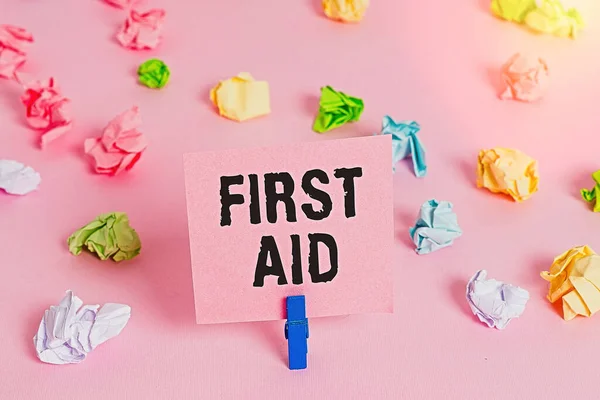 Text sign showing First Aid. Conceptual photo Practise of healing small cuts that no need for medical training Colored crumpled papers empty reminder pink floor background clothespin.