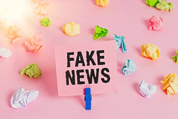 Tekstskilt som viser Fake News. Begrepsfoto som gir informasjon som viser at det ikke er sant på de fargede, krøllede avisene tomme, rosa bakgrunnsklær i purpur . – stockfoto