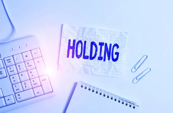 Handschrifttekst Holding. Concept betekent voorraden eigendom en andere financiële activa in iemands bezit Witte pc toetsenbord met lege nota papier boven witte achtergrond. — Stockfoto
