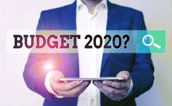 Word writing text Budget 2020 Question. Business concept for estimate of income and expenditure for next year Man in the blue suite and white shirt holds mobile phone in the hand.