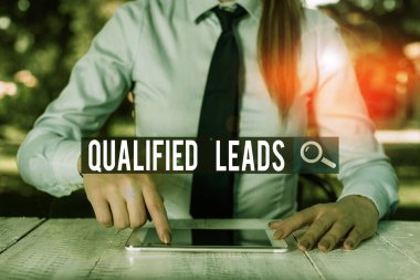 Writing note showing Qualified Leads. Business photo showcasing lead judged likely to become a customer compared to other Female business person sitting by table and holding mobile phone.