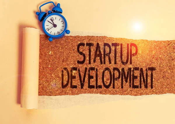 Schrijfbriefje met Startup Development. Zakelijke foto showcasing efficiënt ontwikkelen en valideren schaalbaar business model Alarm klok en gescheurd karton op een houten klassieke tafel achtergrond. — Stockfoto