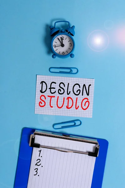 Word writing text Design Studio. Business concept for workplace for designers and artisans engaged in conceiving Alarm clock clipboard squared blank paper sheet clips colored background. — Stockfoto