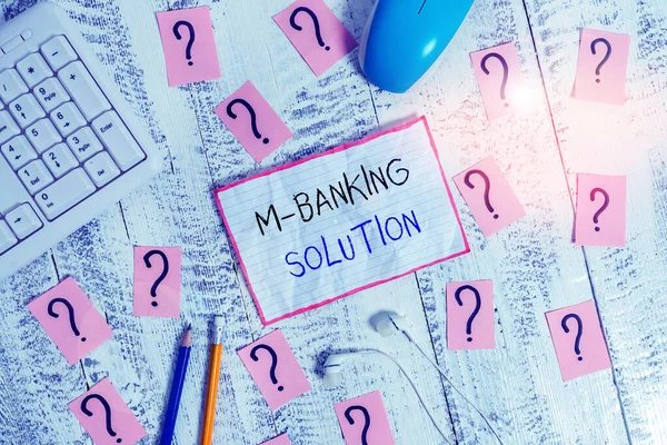 Handwriting text M Banking Solution. Concept meaning accessed banking through an application on the smartphone Writing tools, computer stuff and math book sheet on top of wooden table.