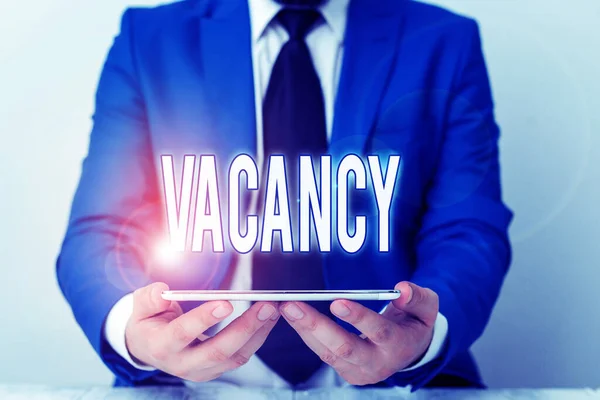 Ordskrivning text Vacancy. Affärsidé för tillgänglig betald plats i små eller stora företag State of being vacant Affärsman i blå svit med slips håller laptop i händerna. — Stockfoto