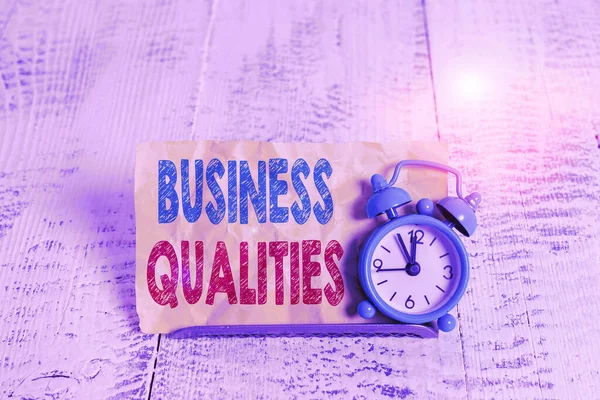 Word writing text Business Qualities. Business concept for meeting the needs and expectations of customers Mini blue alarm clock stand tilted above buffer wire in front of notepaper.