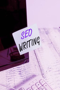 El yazısı Seo Yazma. Konsept, arama motorlarının dikkatini beyaz klavyenin yanındaki siyah bilgisayar monitörü ekranına bantlanmış özel kelime gösterim kağıdıyla çekmek anlamına gelir.