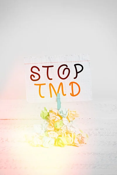 Handwriting text writing Stop Tmd. Concept meaning Prevent the disorder or problem affecting the chewing muscles Reminder pile colored crumpled paper clothespin reminder white wooden space.