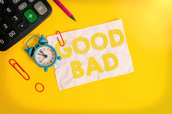 Handwriting text writing Good Bad. Concept meaning to seem to be going to have a good or bad result Life choices Alarm clock clips note rubber band calculator pencil colored background.