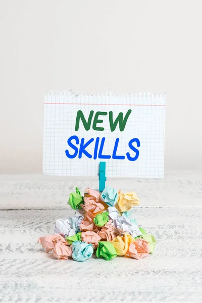 Text sign showing New Skills. Conceptual photo Recently Acquired Learned Abilities Knowledge Competences Reminder pile colored crumpled paper clothespin reminder white wooden space.