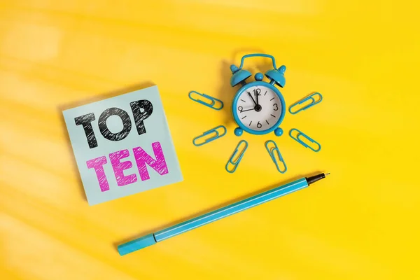 Writing note showing Top Ten. Business photo showcasing the ten most popular songs or recordings in the popular music charts Metal alarm clock wakeup clips ballpoint notepad colored background. — Stock Photo, Image