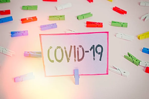 Een briefje met Covid19 erop. Zakelijke foto showcasing milde tot ernstige respiratoire ziekte die wordt veroorzaakt door een coronavirus gekleurde wasknijpers lege herinnering roze vloer kantoor pin. — Stockfoto