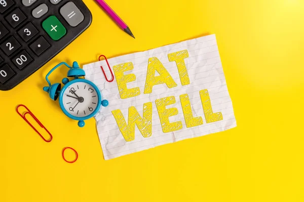 Handwriting text writing Eat Well. Concept meaning Practice of eating only foods that are whole and not processed Alarm clock clips note rubber band calculator pencil colored background.