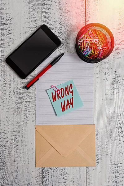 Word writing text Wrong Way. Business concept for taking an unsuitable or undesirable manners or direction Smartphone paper sheet clips holder pen envelope note wooden background.