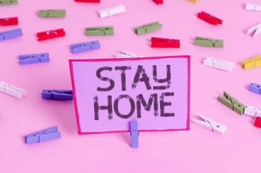 Stay Home 'u gösteren bir not yazıyorum. İş fotoğraflarının sergilenmesi dışarı çıkmamak ve evde veya evde kalmamak. Renkli çamaşır iğnesi kağıtları boş, pembe zemin ofis rozeti..