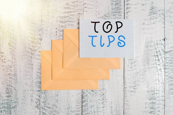 Handwriting text Top Tips. Concept meaning a small but particularly useful piece of practical advice Three envelopes around ruled paper sheet old wooden vintage background.