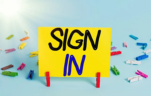 Conceptual hand writing showing Sign In. Business photo text to write your name on a form when entering or leaving a place Colored clothespin rectangle shaped paper blue background.