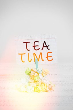 Çay Zamanı 'nı yazan el yazısı metinleri. Kavram, öğleden sonra bazı gösterimlerin küçük bir yemek yediği, renkli, buruşmuş kağıt çamaşır mandalının beyaz ahşap uzayı hatırlattığı zaman anlamına gelir..