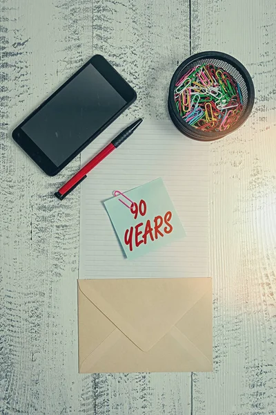Texte écrit 90 ans. Concept d'entreprise pour se souvenir ou honorer jour spécial pour être 90 ans d'existence Smartphone porte-trombones papier stylo enveloppe note arrière-plan en bois . — Photo