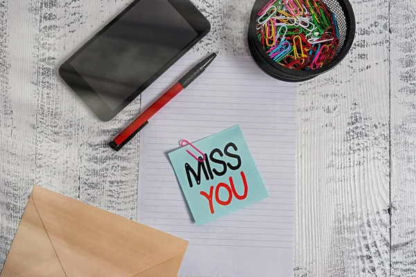 Handwriting text Miss You. Concept meaning Feeling sad because you are not here anymore loving message Smartphone paper sheet clips holder pen envelope note wooden background.