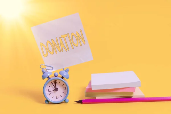 Text sign showing Donation. Conceptual photo something that is given to a charity, especially a sum of money Alarm clock blank pencil sticky note stacked notepads colored background.