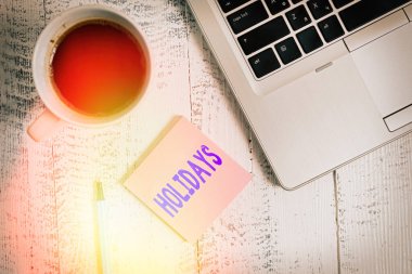 Text sign showing Holidays. Conceptual photo an extended period of leisure and recreation spent away from home Trendy metallic laptop blank sticky pad coffee cup pen lying vintage table. clipart