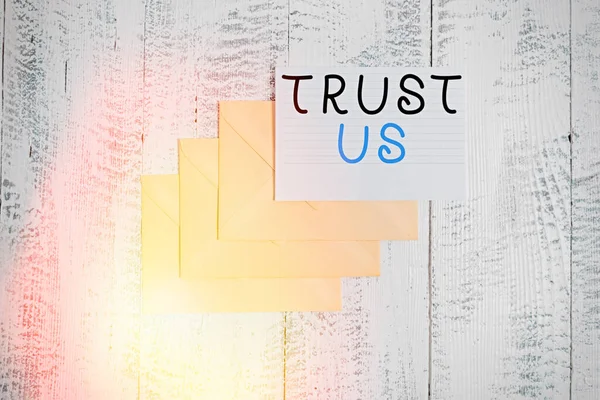 Handwriting text Trust Us. Concept meaning to believe that someone is good and honest and will not harm Three envelopes around ruled paper sheet old wooden vintage background.