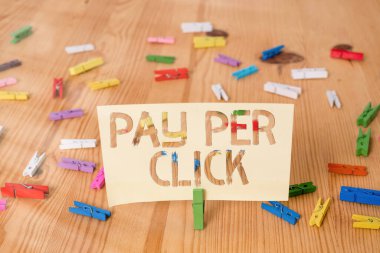 Tıklama başına Ödeme 'yi gösteren mesaj işareti. Renkli çamaşır iğnesi kağıtları boş hatırlatıcı ahşap zemin ofis ödemelerinin yapıldığı kavramsal fotoğraf internet pazarlaması.