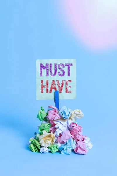 Text sign showing Must Have. Conceptual photo something modern that many showing want to have Essential item Reminder pile colored crumpled paper clothespin reminder blue background.