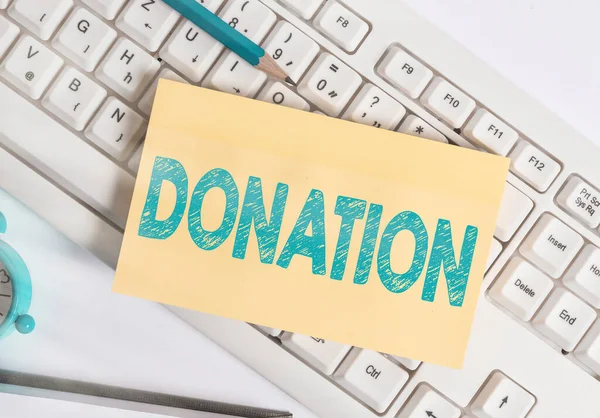 Writing note showing Donation. Business photo showcasing something that is given to a charity, especially a sum of money White pc keyboard note paper and paper clips above white background.