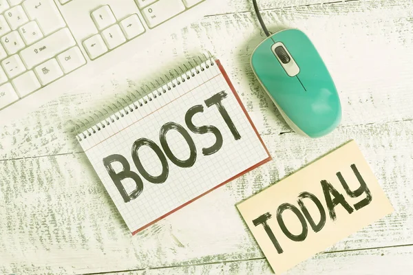 Writing note showing Boost. Business photo showcasing a source of help or encouragement leading to increase or improvement Writing equipments and computer stuff placed on wooden table.