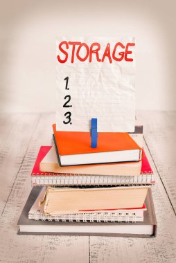 Depo 'yu gösteren bir not yazıyorum. İş fotoğrafı gösterimi depolama eylemi ileride kullanılacak şeyler için güvenli bir şeyler istiflenmiş kitaplar dizüstü bilgisayar broş rengi hatırlatıcı beyaz ahşap.