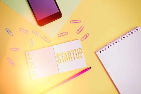 Nota de escritura que muestra Startup. Foto de negocios mostrando la acción de poner algo en movimiento recién establecido negocio Cuadrado en blanco pegajosos bloc de notas lápiz teléfono inteligente hoja color fondo . — Foto de Stock